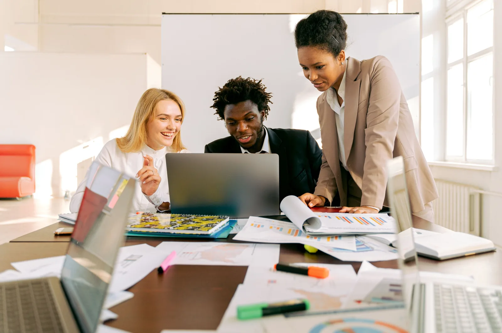 Three colleagues reviewing a laptop and printed plans in a bright office